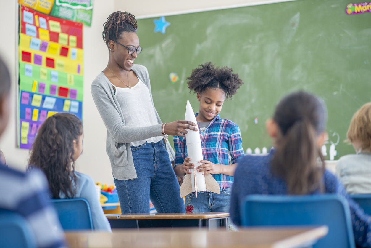A student and teacher hold a model rocket in front of the class. 