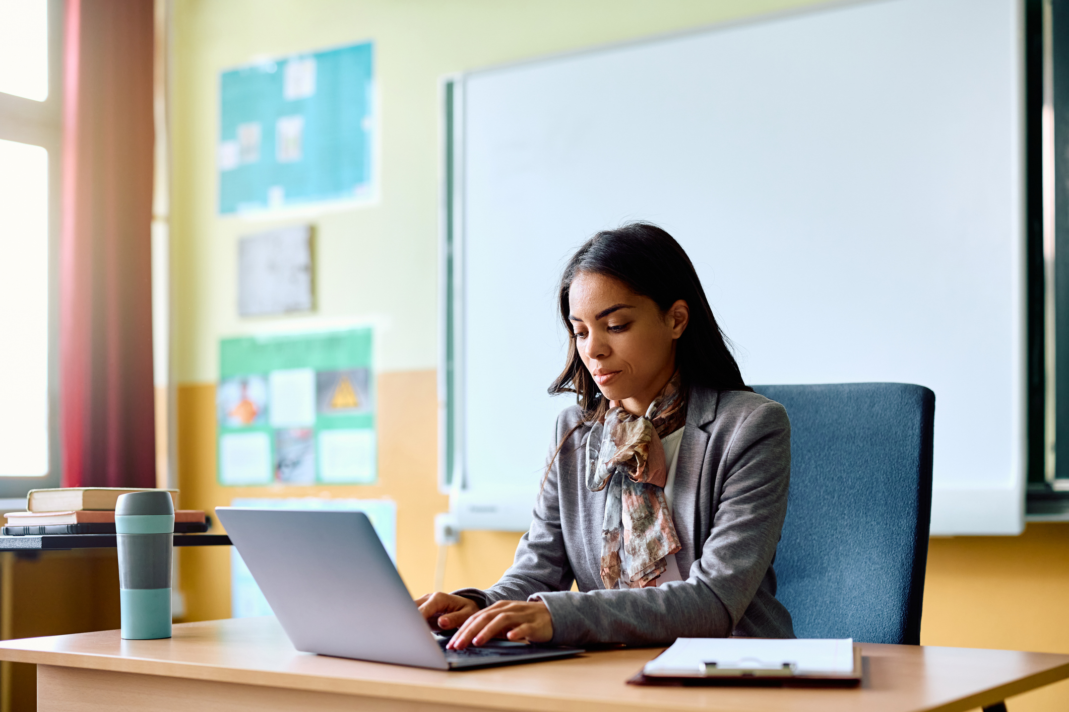 A teacher uses a laptop at a desk to access a student data management system.
